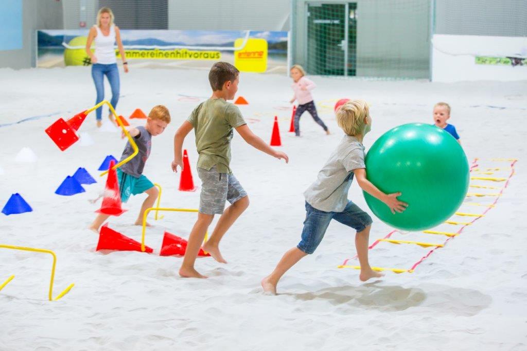 Kinder spielen mit einem großen grünen Ball im Sand der Beachhalle Klagenfurt